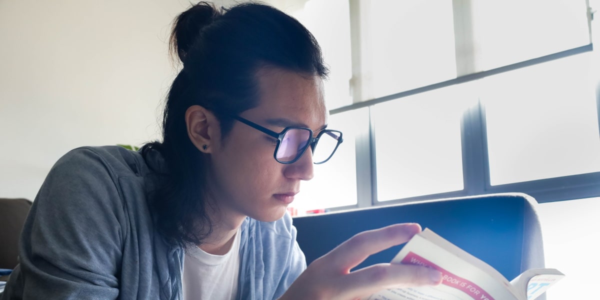 person reading book with reading glasses in oversized frame