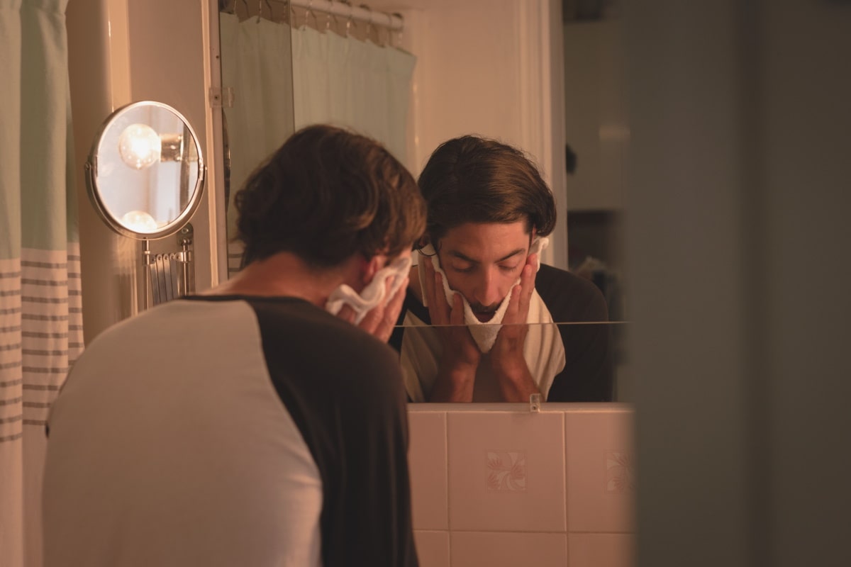 man relieving itchy eyes with hot compress in the bathroom