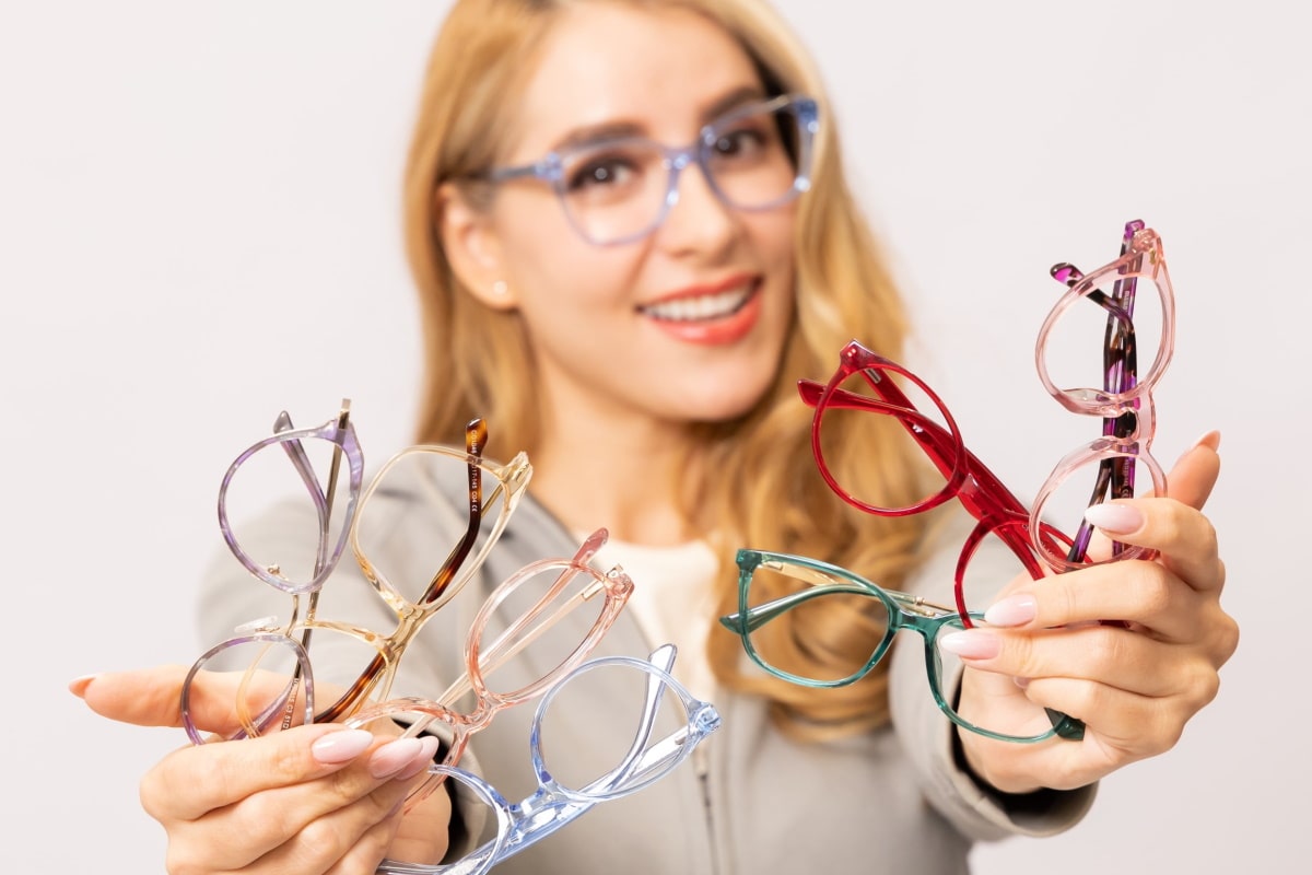 woman wearing eyeglasses holding a few pairs of eyeglasses frames