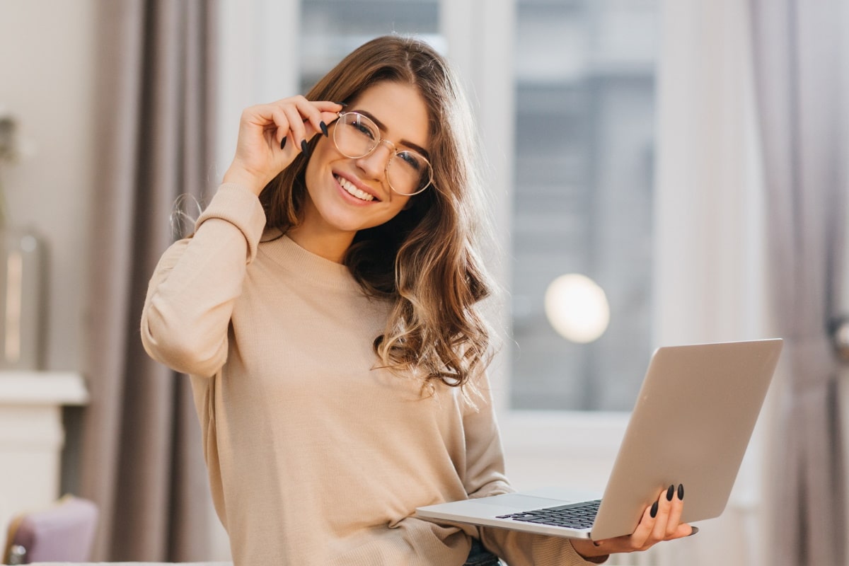 smiling woman wearing a pair of eyeglasses holding a laptop