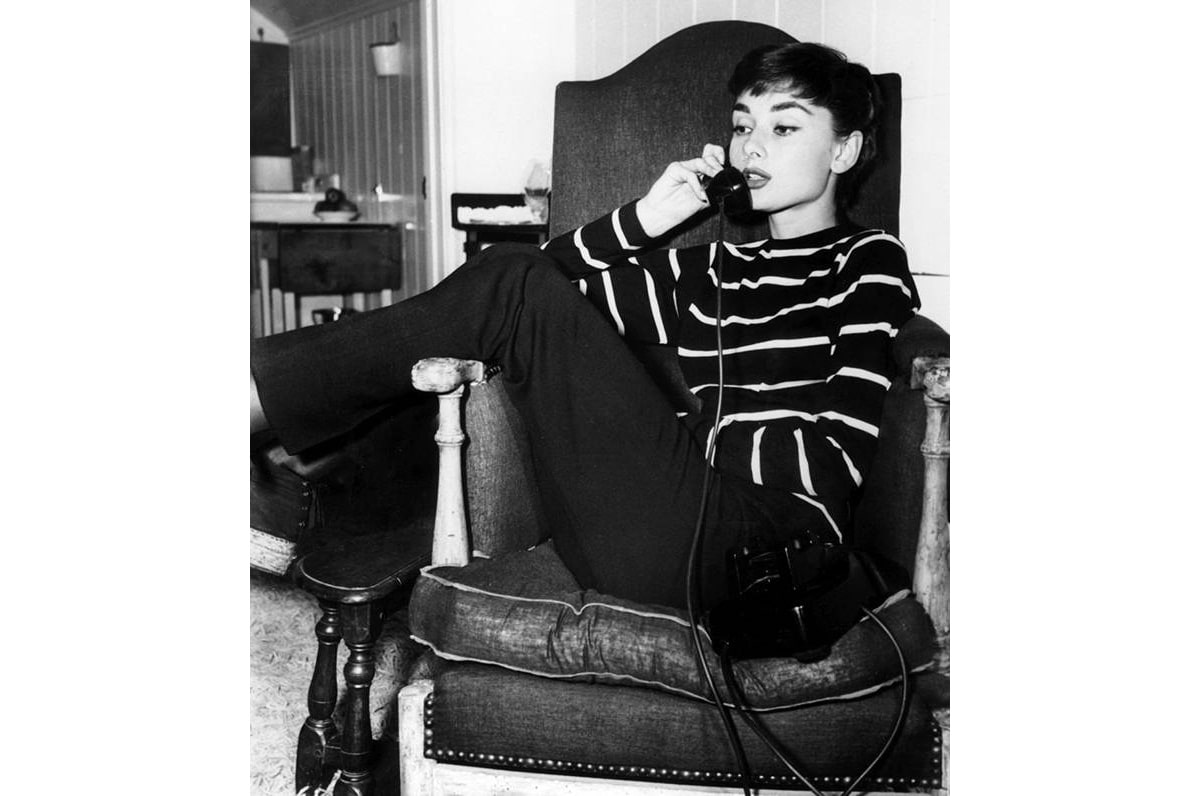 Audrey Hepburn speaking on a phone wearing a striped top and black slack