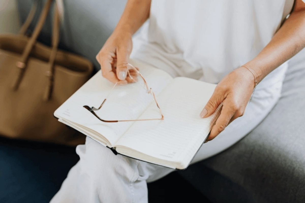 person placing a pair of glasses on top of an opened book