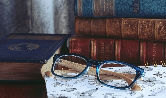 a pair of reading glasses in blue frame placed beside books
