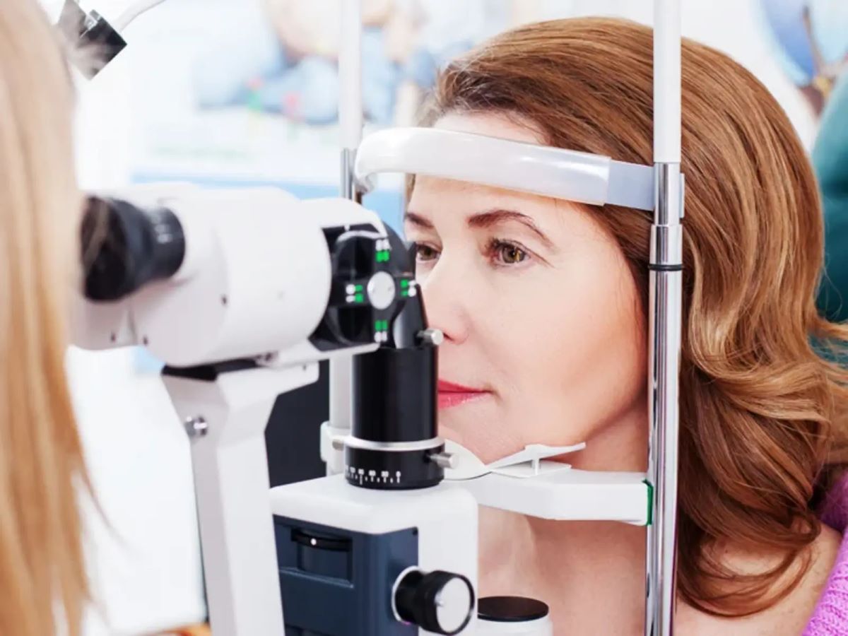 a woman resting her chin on a slit lamp microscope