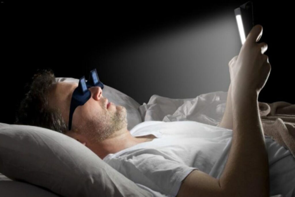 man laying on a bed operating phone while wearing lazy glasses