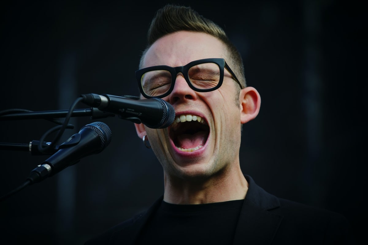 a singer wearing a pair of black glasses while singing into a mic