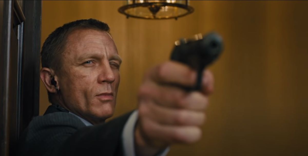 daniel craig winking as james bond while aiming a gun