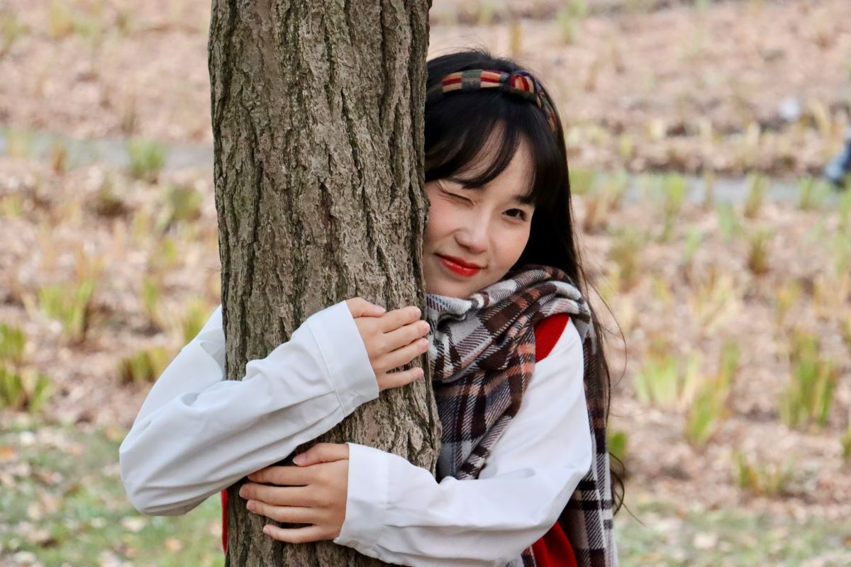 Japanese woman winking while hugging a tree