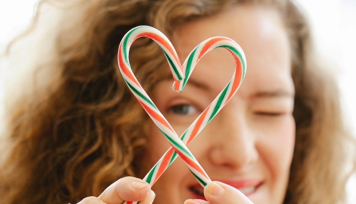 woman winking holding candy canes in a way that forms a heart shape