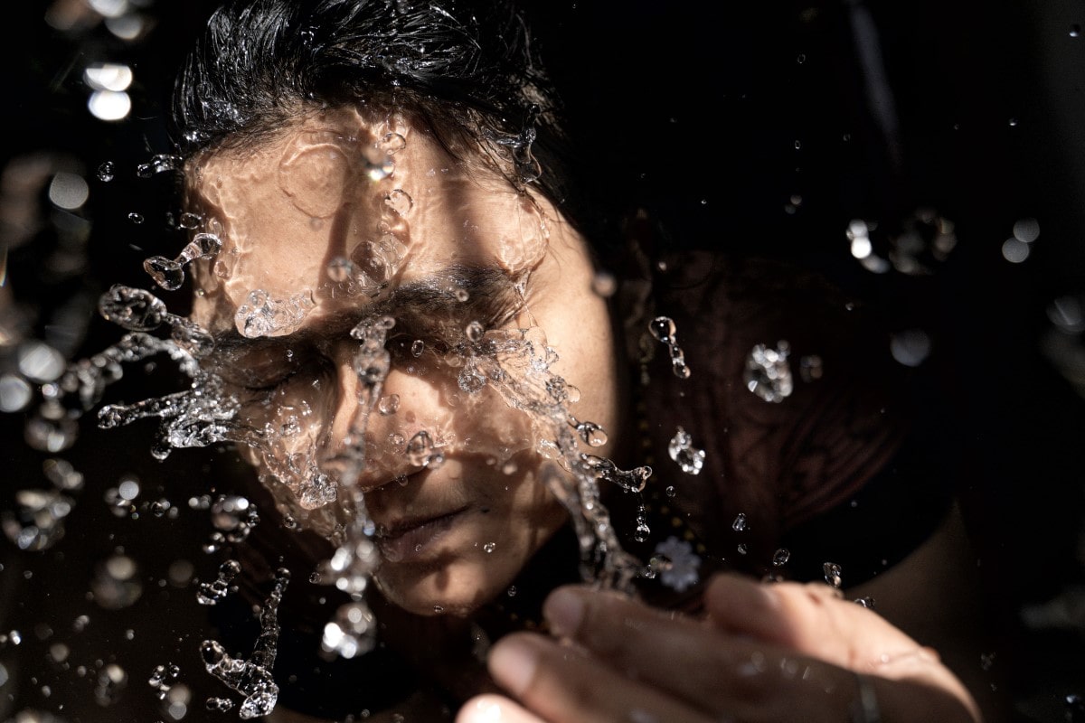 a person splashing water to their face to clean their eyelids