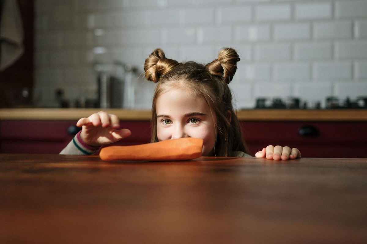 a kid eyeing on a peeled carrot placed on a countertop