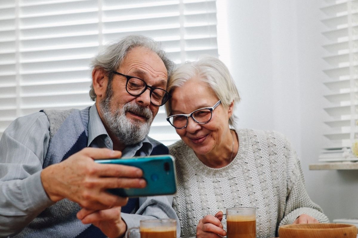 old couple with glasses taking selfie on white background