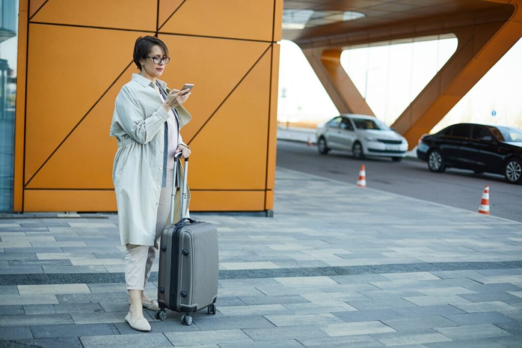 bespectacled woman and her luggage looking at her phone