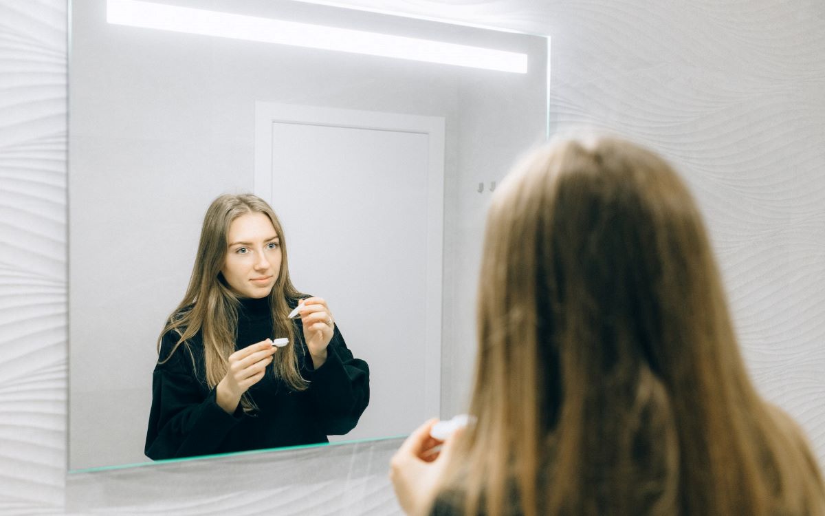 woman putting on contact lenses in front of a mirror