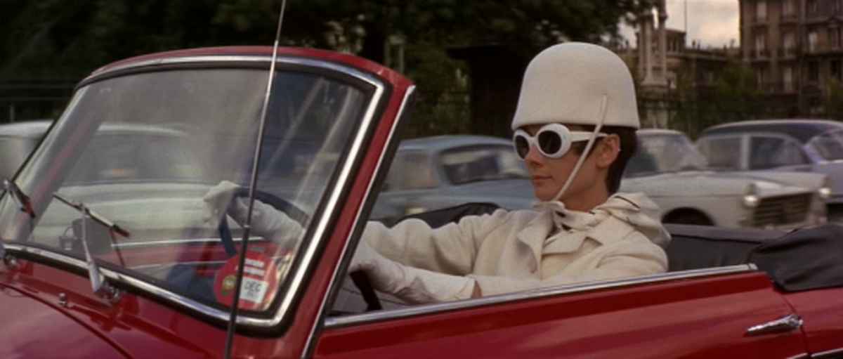audrey hepburn wears white sunglasses while driving a red car in how to steal a million