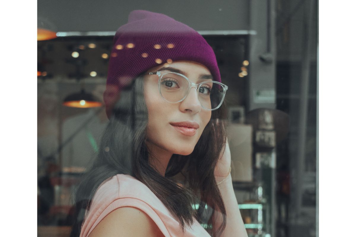woman wears clear glasses with purple beany