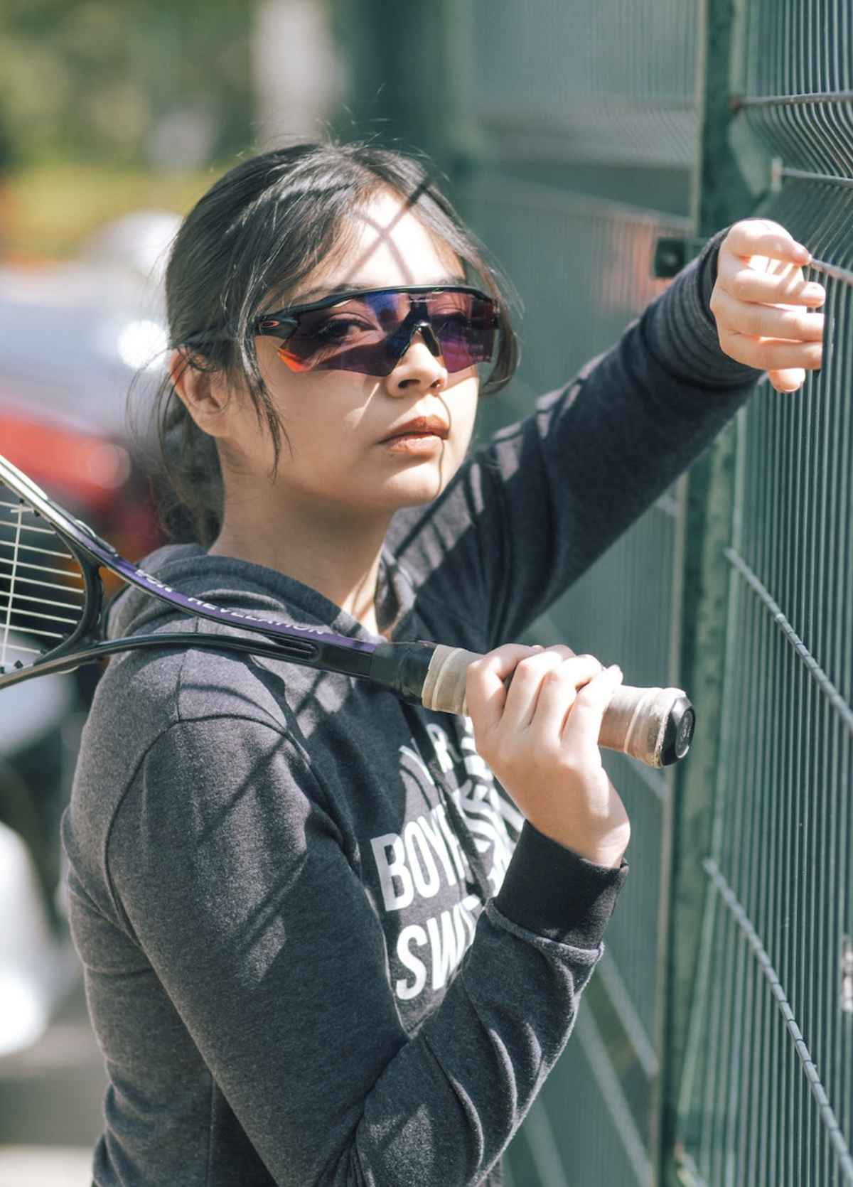 woman wears wraparound sunglasses while holding a tennis racket