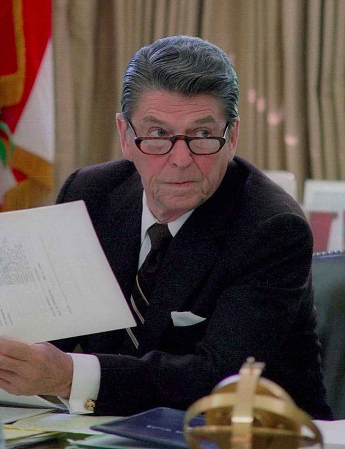 President Ronald Reagan wearing glasses while working at his desk in the oval office