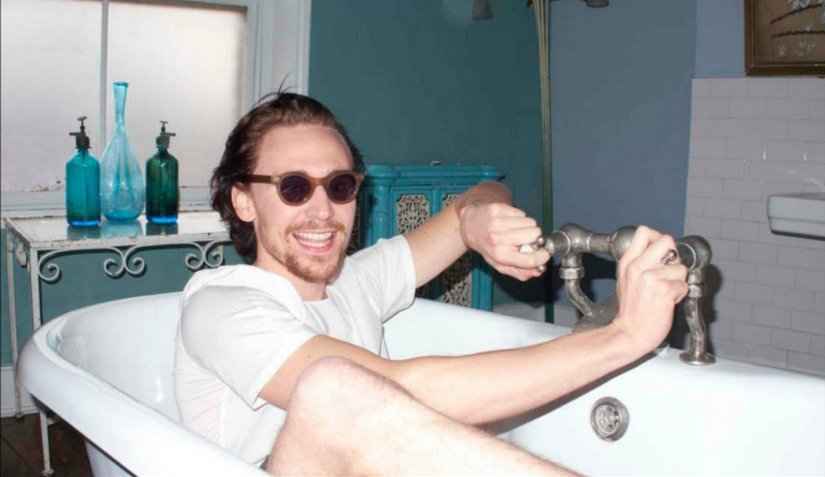 tom hiddleston in a bathtub wears clear round acetate sunglasses for the 1883 magazine photoshoot