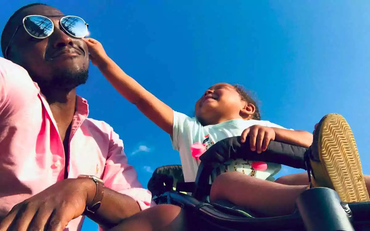 a kid reaching out to grab a sunglasses worn on the father's face